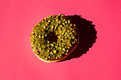 Draufsicht auf einen mit grünem Zucker bestrichenen Donut mit Nüssen auf rosa Hintergrund