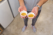 Crop anonymous male barista in casual wear showing mugs of hot espresso while standing in light modern coffee house during work