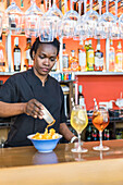 Focused African American female bartender serving tasty mussels snacks on counter with alcohol cocktails in bar