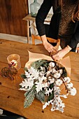 Crop unrecognizable female florist standing arranging Christmas bouquet on wooden table