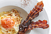 Overhead view of tasty eggs with fried bacon strips on plate