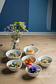 High angle of assorted tasty dishes in ceramic bowls placed on wooden floor near glass vase with fresh blooming flowers