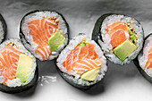From above set of tasty Futomaki Norwegian sushi rolls with salmon and avocado served on plate in light studio