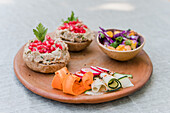 Schüssel mit frischem Salat auf Holzteller mit geschnittenem Gemüse und belegten Brötchen mit Pilzpastete, vorbereitet für ein vegetarisches Mittagessen