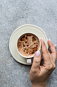 Top view of the ceramic cup of cappuccino with foam in the woman's hands