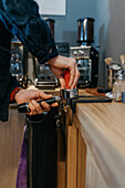 Crop faceless barista standing at table and preparing fresh aromatic coffee while working in cafeteria in daytime