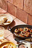 Appetizing grilled shrimps with herbs prepared in pan placed near bread and spices on table with fork and spoon