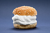 Halves of burger bun with sesame and sweet whipped cream placed against blue background