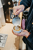 Anonymer Barista gießt von oben Milch in eine Tasse Kaffee, während er in einer Cafeteria einen Milchkaffee zubereitet