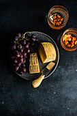 Black stone plate with cheeses, raw tasty grape and glasses of wine on dark concrete table