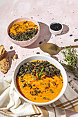 From above of appetizing homemade pumpkin purees with seeds and herbs in bowls placed on table near crispy bread slices in kitchen