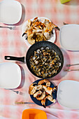 Top view of frying pan with fried mollusks served on table with crab claws and white plates in light kitchen