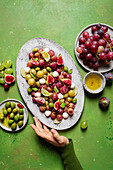 From above cropped unrecognizable cook holding plate with fresh ripe grapes, olives, figs and mozzarella seasonal christmas salad placed on plate on green tabletop background