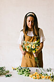 Adult Hispanic female florist in apron arranging bouquet of assorted gentle fresh flowers against white background