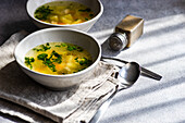 Hühnersuppe mit Gemüse, serviert in Schalen auf einem weißen Betontisch, bereit zum Abendessen