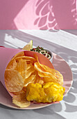 Appetizing fried chips and fish in paper wrapping served on plate with sauce on table with bright sunlight in cafe