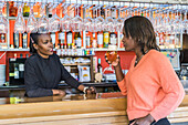 Cheerful black female barkeeper serving glass of refreshing beer for client in bar