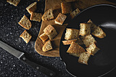 Pieces of crispy bread in bowl near wheat spikes on black textile in room