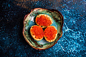 From above bruschetta with red caviar on ceramic plate on stone table