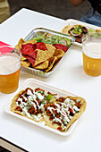 From above of appetizing nachos with salad and tacos with sauce on plates served with glasses of beer in restaurant