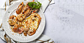 From above appetizing fried eggs with king prawns served on white plate with green herbs and seasoning on towel in light kitchen