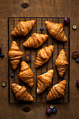 Blick von oben auf leckere süße, frisch gebackene Croissants mit Früchten auf einem Metallgitter auf einem Holztisch