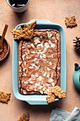 Top view of tasty baked brownie with almond flakes in baking tray with cookies placed on table with cocoa powder