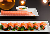 Fresh raw salmon fillet placed near sushi rolls with rice served on plate