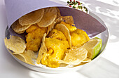 Appetitlich gebratene Pommes frites und Fisch in Papierverpackung auf einem Teller mit Soße auf einem Tisch mit hellem Sonnenlicht in einem Café serviert