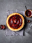 From above of yummy homemade sweet cheesecake placed against jar with sauces and bowl of jam on gray table