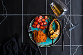 top view of Salmon steak with spicy carrot and cherry tomatoes served with a glass of dry white wine on black tiled table