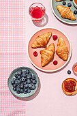 Von oben der Zusammensetzung der plated mit frisch gebackenen süßen Croissants serviert mit Beeren und Marmelade auf rosa Tisch platziert