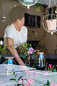 Side view of crop anonymous female florist standing with green plant in glass terrarium in floral shop