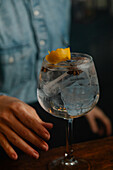 Soft focus of cropped unrecognizable female barkeeper putting with tongs lemon zest into glass with ice cubes while making cocktail in bar