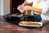 Cropped unrecognizable adult woman pouring batter on hot electric griddle while cooking pancakes at counter in modern kitchen