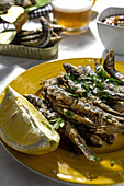 From above of delicious fried anchovies served on plates with lemon and placed on white table with glass of beer