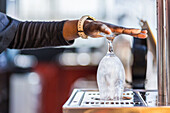 Unrecognizable crop black barman rising glass with water before serving drink in bar