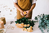 Anonymous female floral designer in apron standing at table and creating floral composition with blooming roses in workshop
