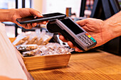 Cropped anonymous woman with fabric bag using smartphone to pay for groceries to vendor while visiting zero waste shop