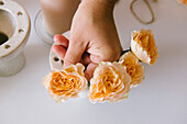 From above of crop anonymous female florist arranging blooming yellow roses in ceramic stand in floral salon