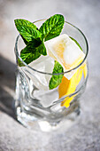 Glass of lemon water with mint on concrete background in sunny day with shadows