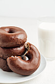 Pile of sweet tasty doughnuts with chocolate glaze placed on plate on white table with glass of milk in light room