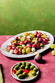 Fresh ripe grapes, olives, figs and mozzarella seasonal christmas salad placed on plate on green and pink tabletop background