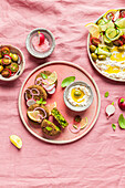 Top view of plate with delicious cream cheese and assorted vegetables placed on napkin near vegan fritters on pink background