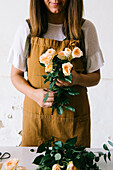 Anonymous adult Hispanic female florist with dark hair in apron arranging bouquet of assorted gentle fresh flowers against white background