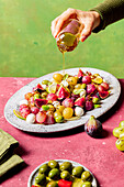 Cropped unrecognizable cook pouring olive oil on plate with fresh ripe grapes, olives, figs and mozzarella seasonal christmas salad placed on plate on green tabletop background
