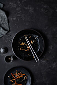 Schwarze leere Schüssel mit Stäbchen und Resten der koreanischen Küche Japchae am Tisch neben vollem Teller