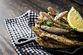 Overhead view of appetizing Fried anchovies with chopped parsley and fresh lemon slice with juicy flesh