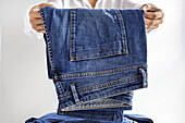 Crop unrecognizable female in white shirt stacking blue jeans in pile of clothes after washing