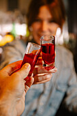 Soft focus of crop unrecognizable female barkeeper clinking with alcoholic red blood shots with faceless person while working in bar